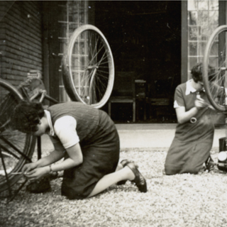 Foto met twee dames, bezig met hun fiets, voor de loggia
